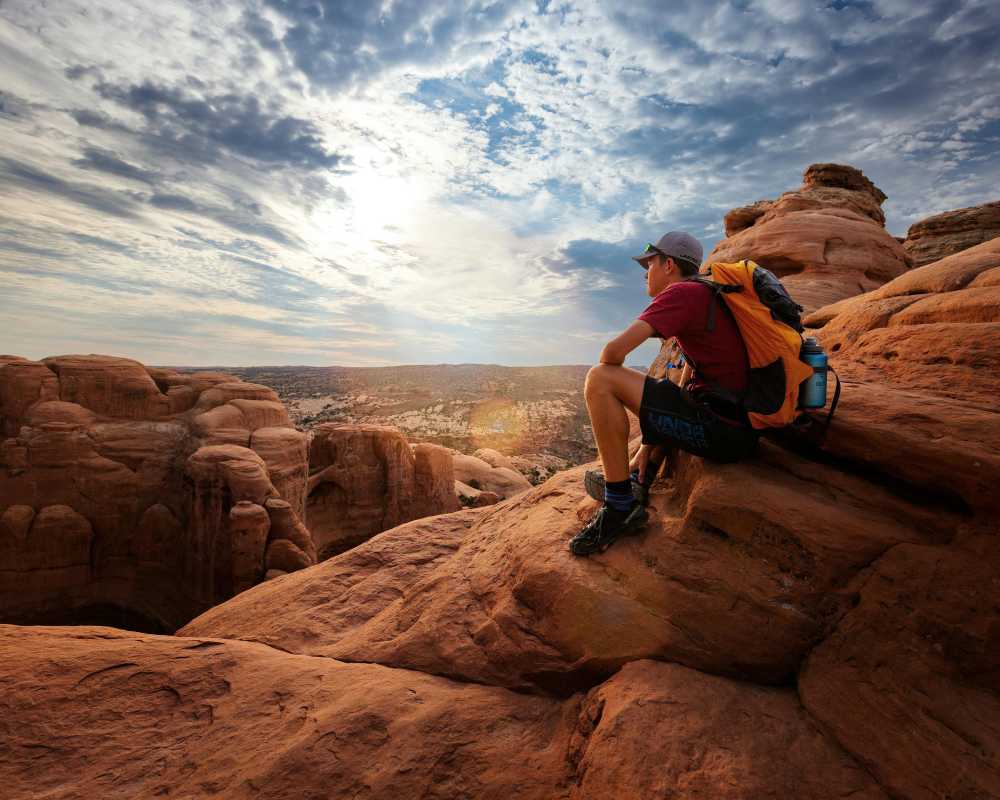 solo hiker, mountain summit, looking at view, Moab Utah, red rocks, backpack, sense of freedom